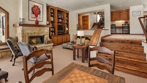 Un soggiorno ampio con camino, arredamento in legno e un angolo cottura visibile attraverso un'apertura.