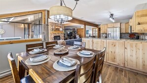 Un comedor con una mesa de madera dispuesta para seis personas, una lámpara colgante y armarios de madera al fondo.