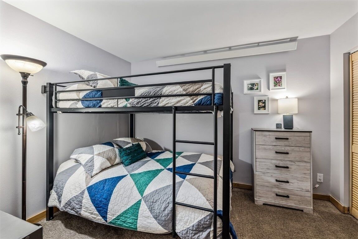 A bunk bed with a geometric-patterned quilt, a bedside lamp, a dresser, and framed pictures on the wall.