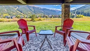 Un patio cubierto con dos sillas Adirondack rojas, una mesita y vistas a un paisaje montañoso.