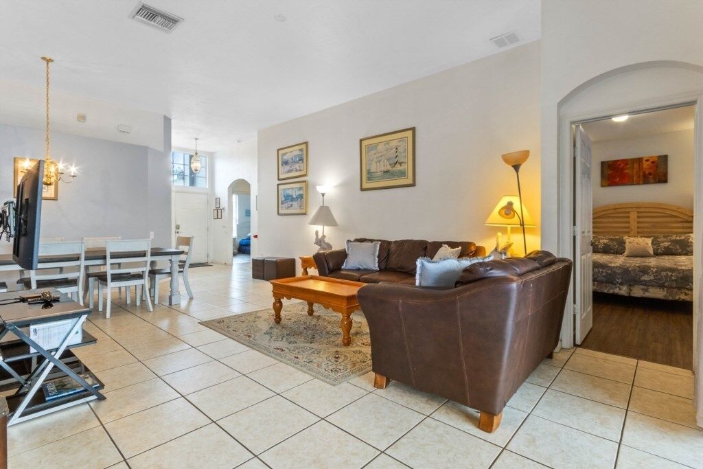 A spacious living room with a brown leather sofa, a wooden coffee table, and a dining area with a white table and chairs.