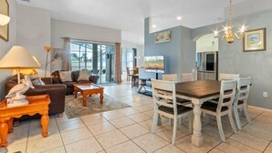 Un grand espace de vie comprenant un canapé, une table basse et une table à manger. On y trouve également un téléviseur et un lustre.