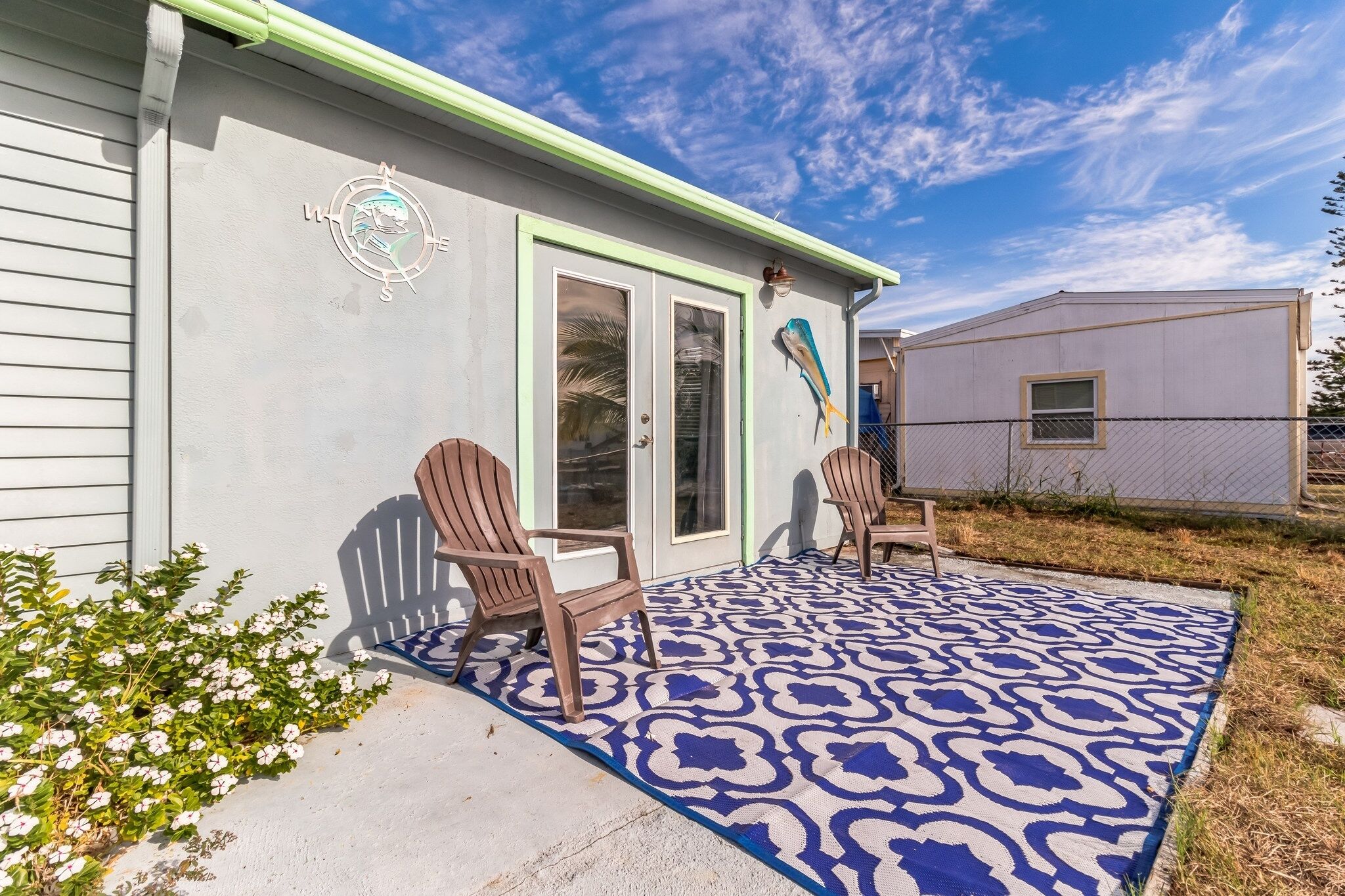 A house with a covered patio, two Adirondack chairs, and a decorative wall sign.