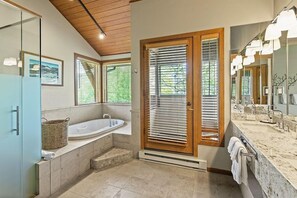 A modern bathroom with a large bathtub, a glass shower enclosure, and a vanity with a large mirror.