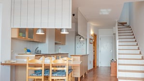 A modern kitchen with wooden cabinets, a dining table with chairs, and a staircase leading to another level. - Casa Noray         . (La Isleta del Moro)