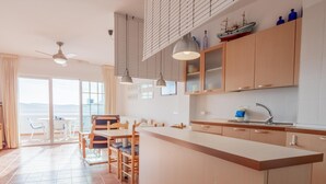 A modern kitchen with a central island, wooden cabinets, and a large window overlooking a scenic view. - Casa Noray         . (La Isleta del Moro)