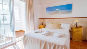 A hotel room with a bed, two bedside tables, a painting of a beach scene, and a view of the sea through a large window. - Casa Noray         . (La Isleta del Moro)
