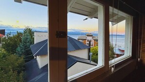 A view from a window overlooking a residential area with houses and a body of water during sunset. - Casa Cocó (San Carlos de Bariloche)