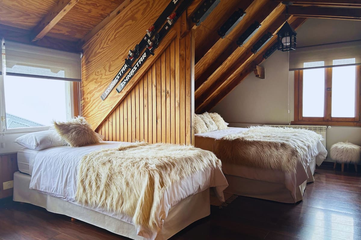 Una habitación con dos camas, vigas de madera, techo inclinado y una ventana.