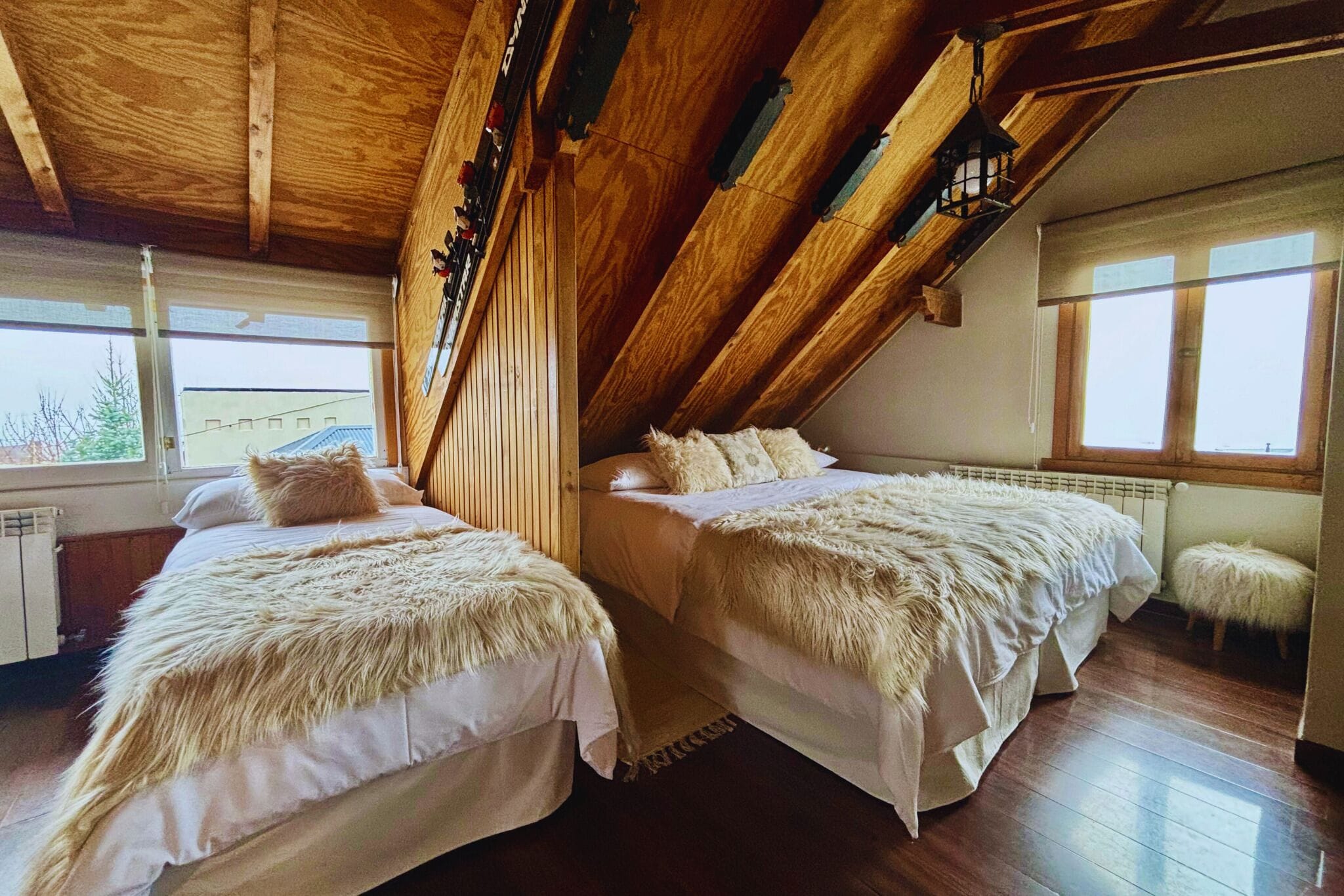 A bedroom with two beds, wooden ceiling beams, and large windows.