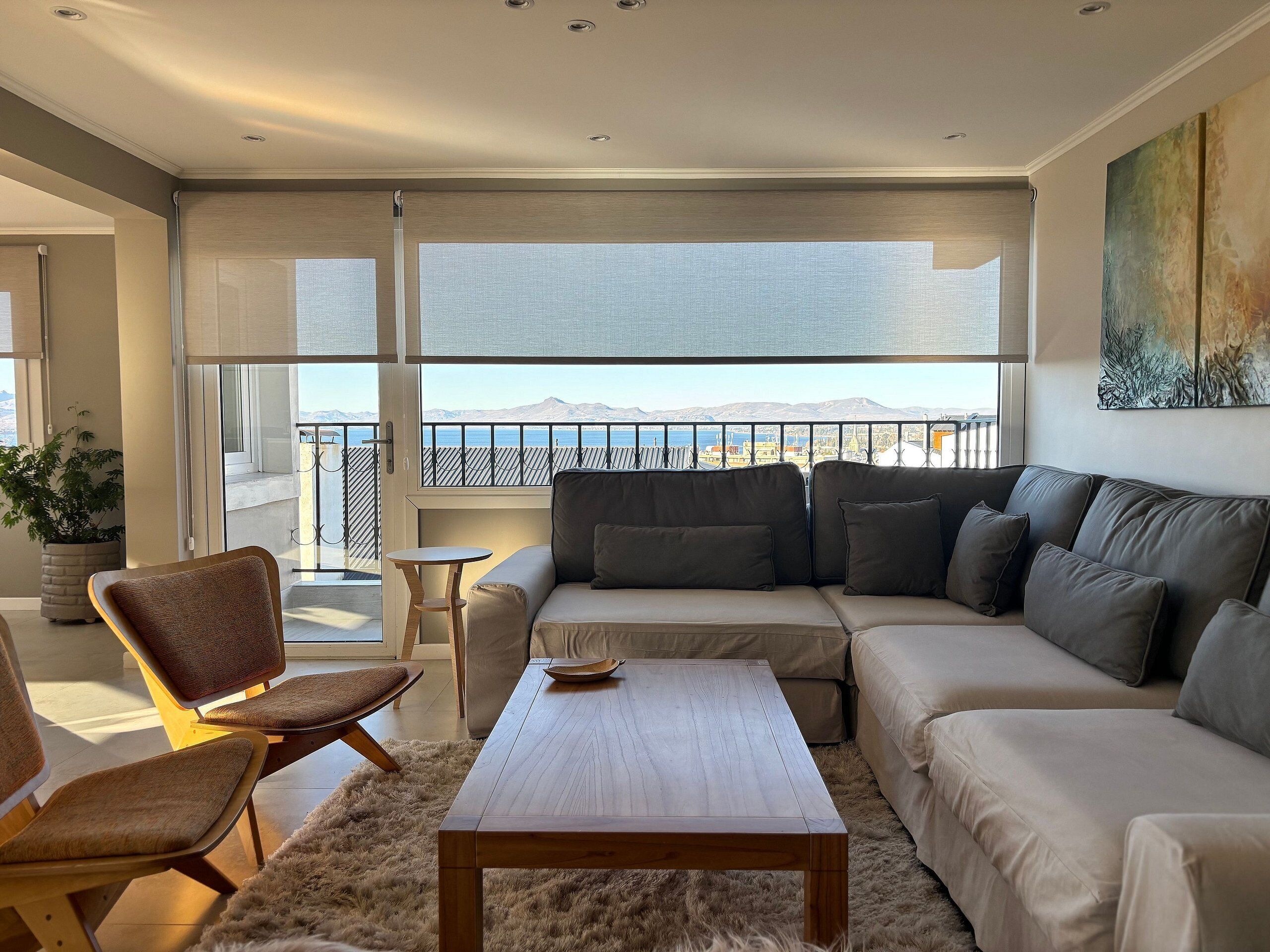 Ein modernes Wohnzimmer mit einer Couch, Sesseln, einem Couchtisch und Meerblick durch große Fenster.