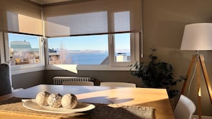 A dining area with a table set for two, a view of the sea, and a lamp in the corner. - Casa Cocó (San Carlos de Bariloche)