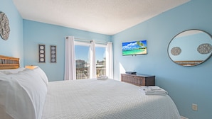 A bedroom with a bed, a TV, a mirror, and a view of the outside. - Lounge around our Texas size pool, barbecuing, and play tennis.  Enjoy the sunse (Port Aransas)