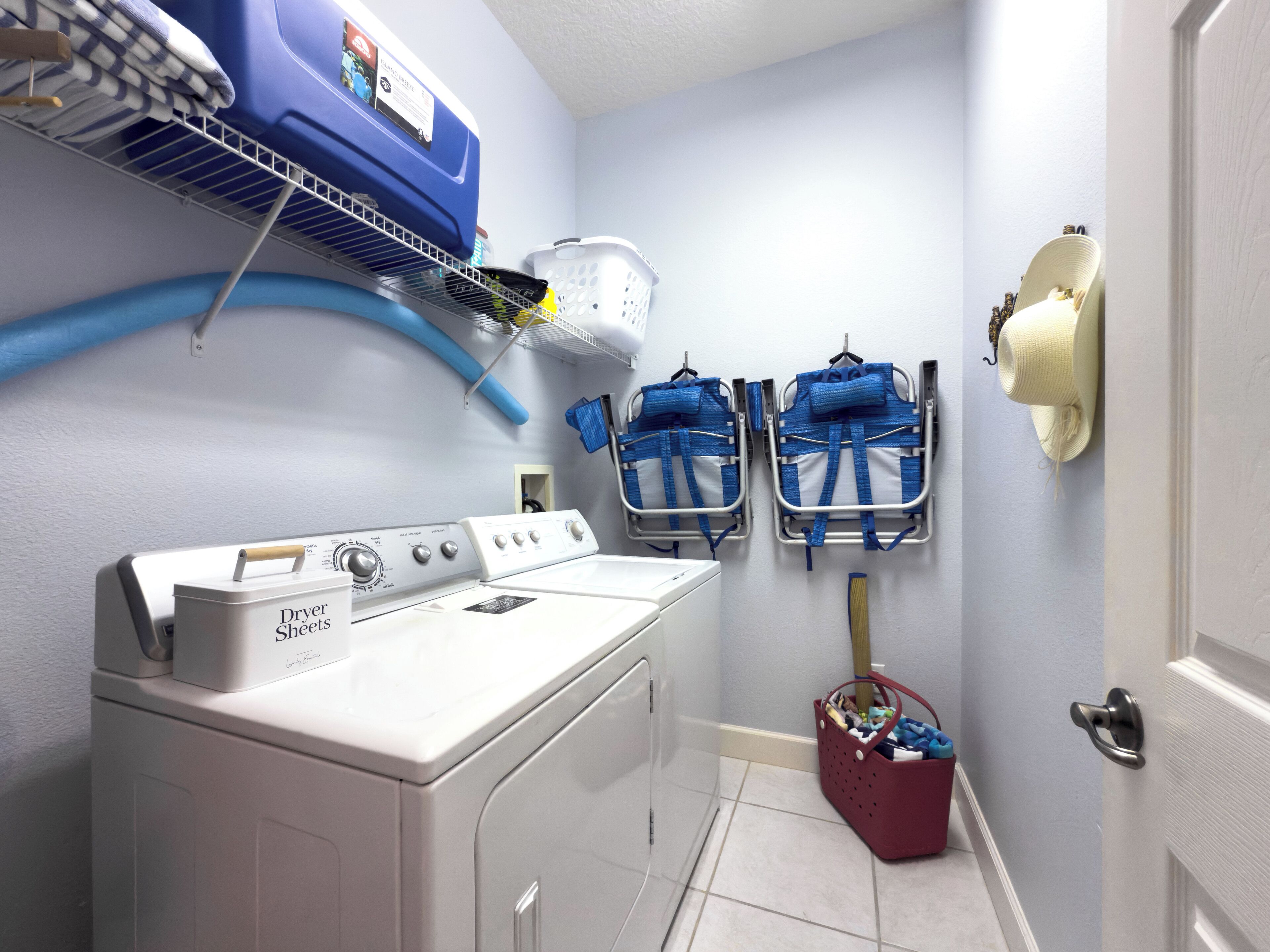 A laundry room with a front-loading washer and dryer, blue laundry baskets, and a red basket with clothes.