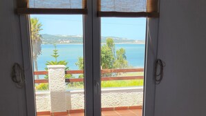 Una habitación con puerta de cristal corredera que da a una terraza con vistas al mar y las colinas.