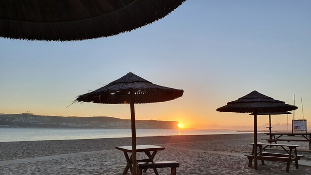 Una playa con dos sombrillas de paja y bancos de madera.