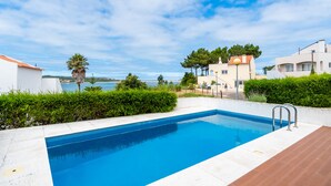 Piscina con vistas claras al mar, rodeada de vegetación y edificios modernos.