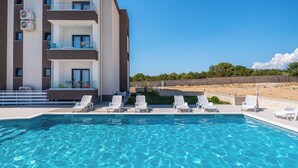 A swimming pool with lounge chairs, a building with balconies, and a clear blue sky. - Deluxe Villa Laura for 8 (Novalja)