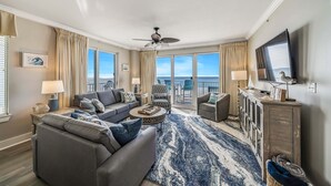 Un salon spacieux avec un grand canapé, une table basse et un téléviseur. Il y a un balcon avec vue sur l’océan.