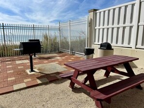 Eine Außenpatio mit Picknicktisch und Grill, umgeben von einem weißen Zaun und Blick auf den Strand.