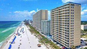 Ein Strandhotel mit mehreren Etagen, ein Sandstrand mit Sonnenschirmen und ein Steg im Hintergrund.