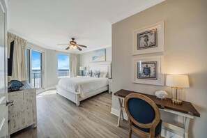 Ein Hotelzimmer mit Bett, Schreibtisch, Stuhl, Deckenventilator und Bildern an der Wand.