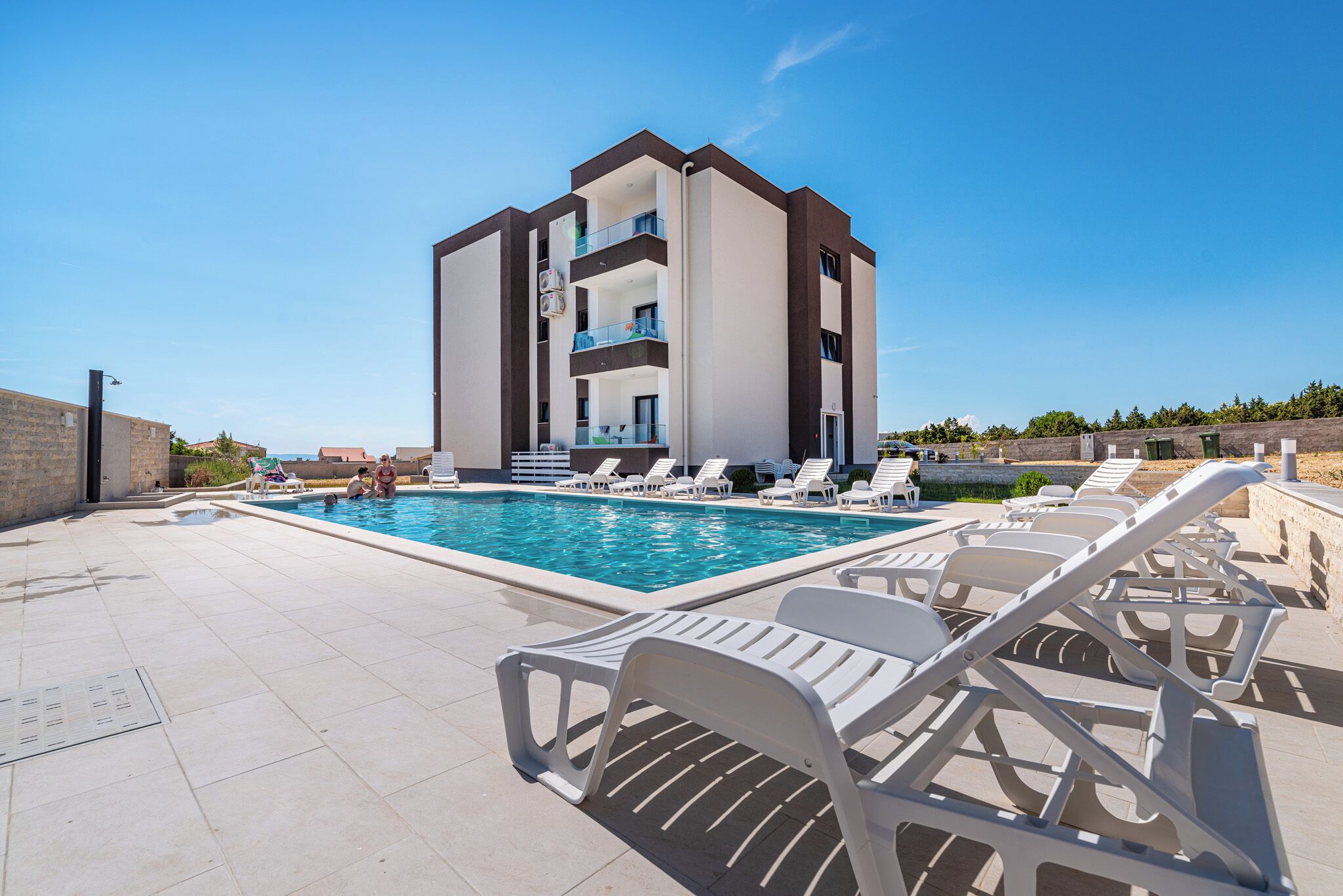 A modern building with a swimming pool, lounge chairs, and a clear blue sky.