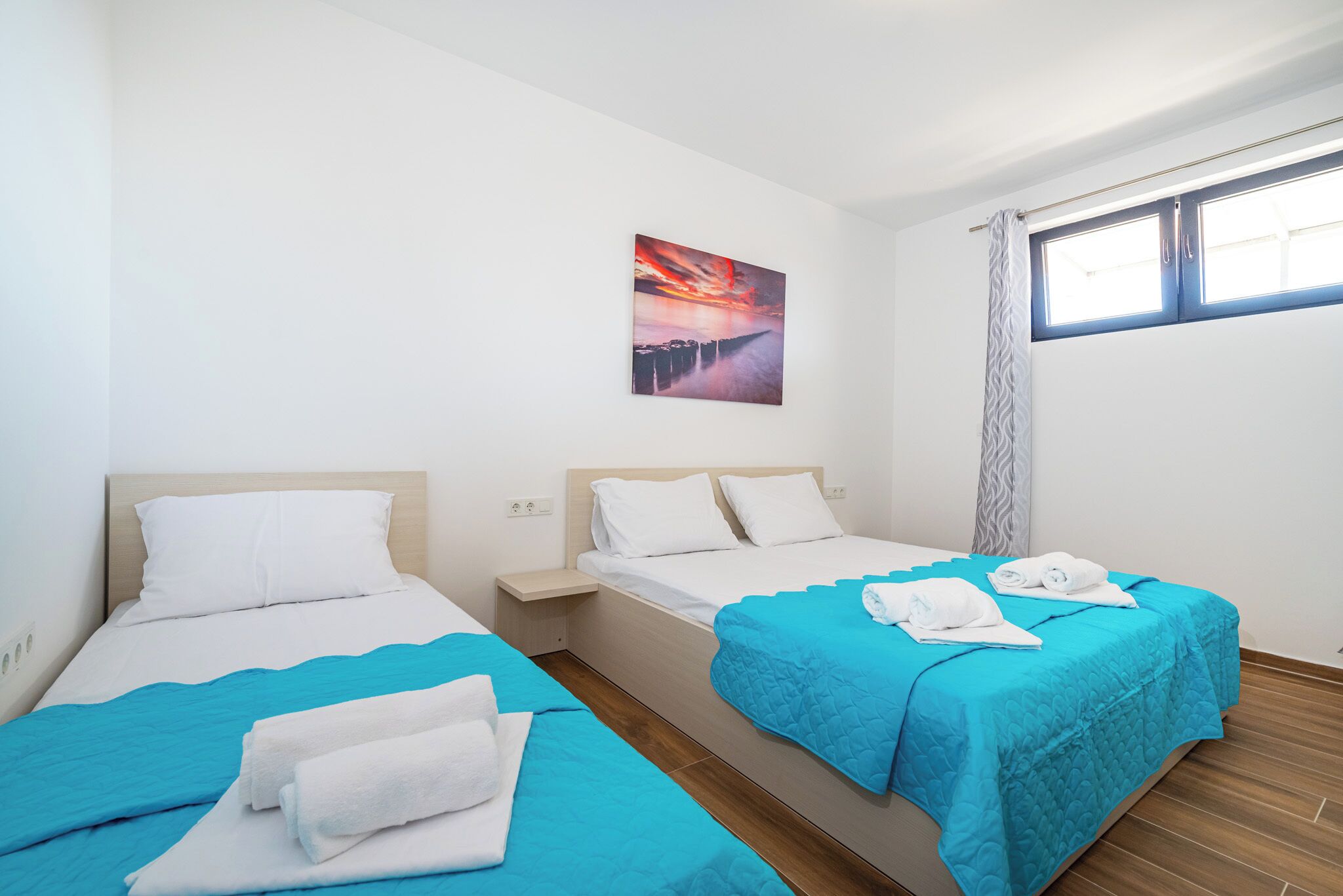 Habitación de hotel con dos camas, un cuadro en la pared y una ventana con cortinas.