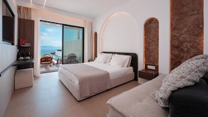 A modern hotel room with a large bed, a sofa, a desk, and a view of the sea. - Muse of Mykonos  (Mykonos)