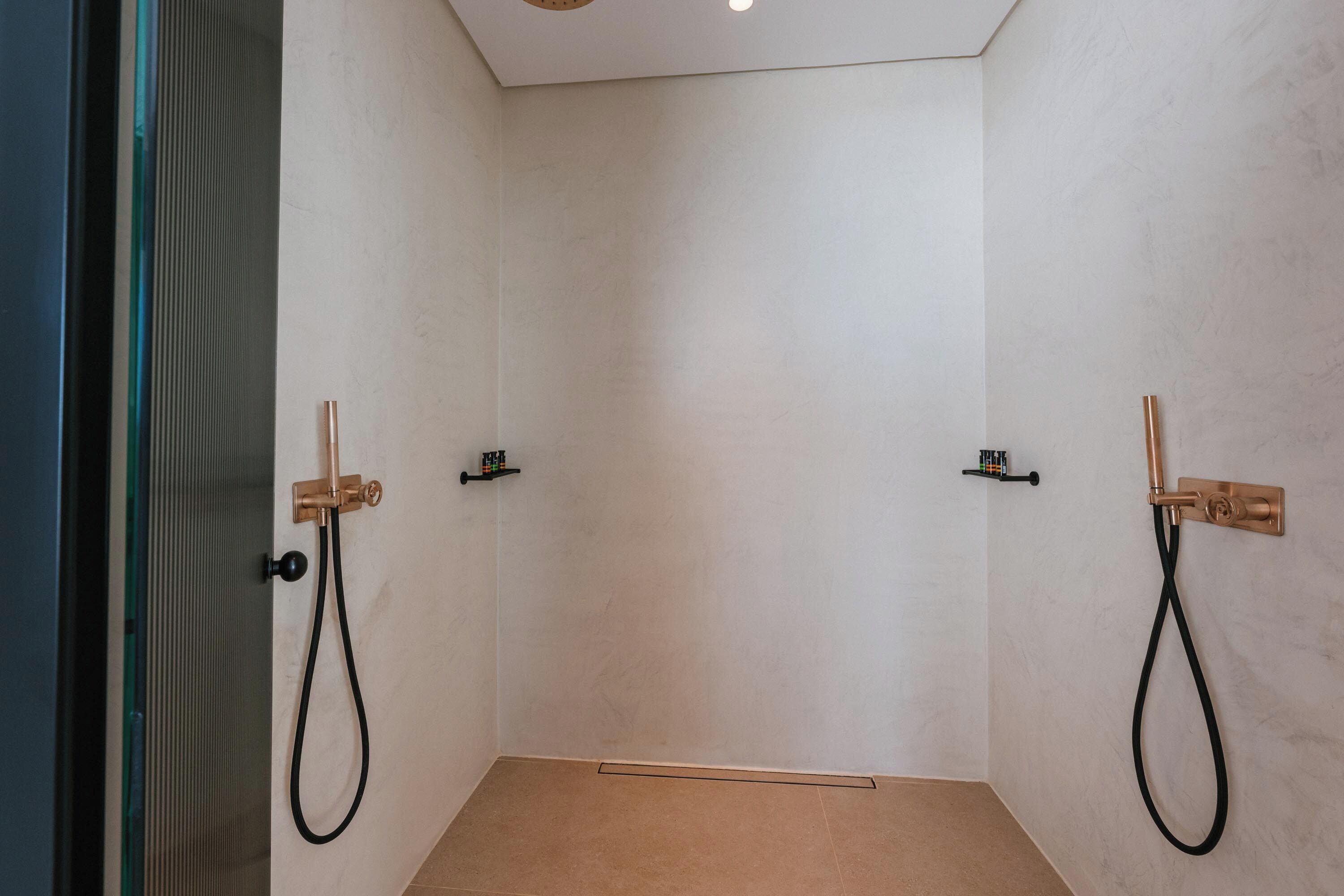 A modern shower room with two showerheads, a glass door, and a tiled floor.
