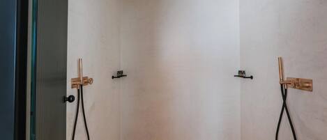 A modern shower room with two showerheads, a glass door, and a tiled floor.