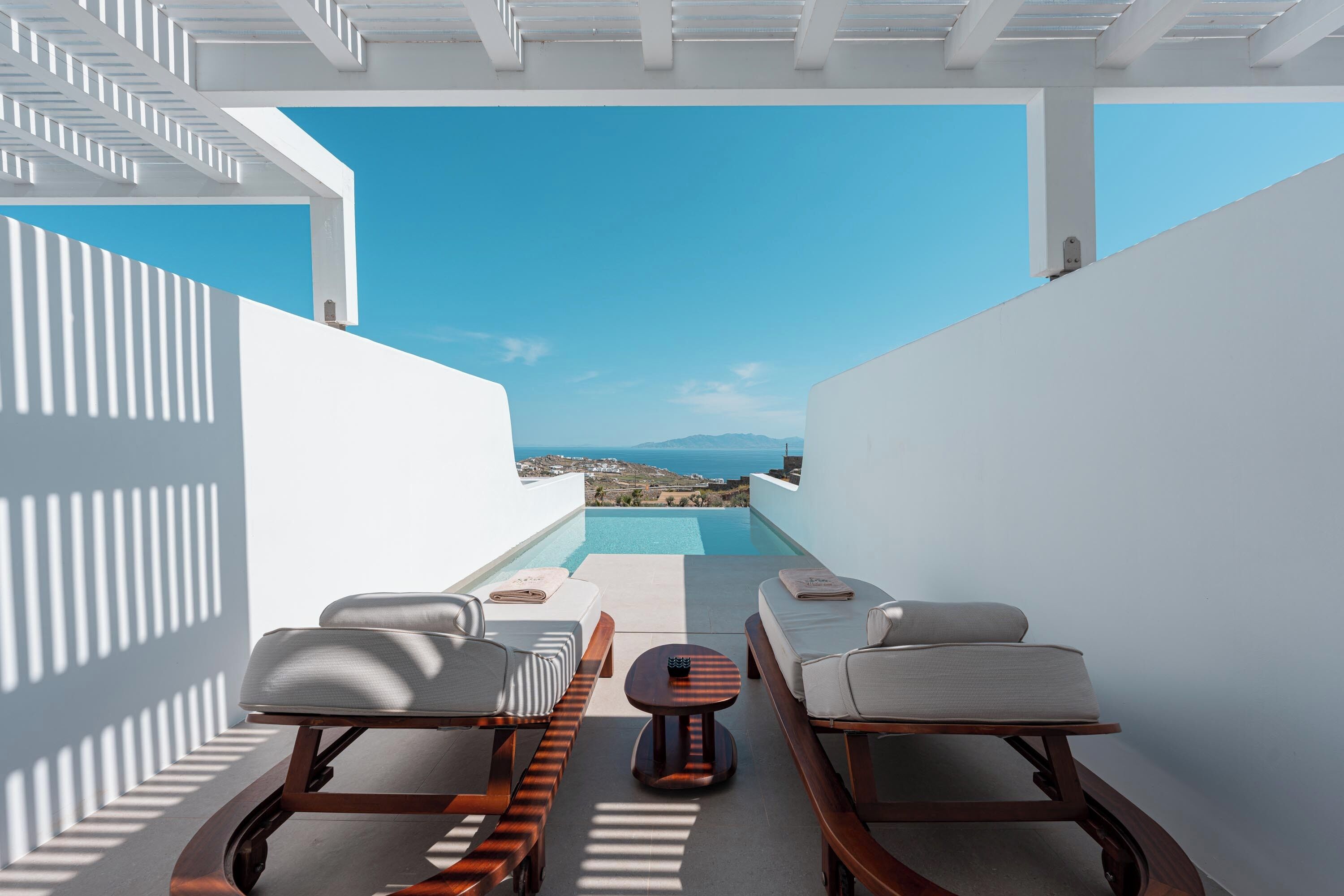 Un área de estar moderna al aire libre con piscina, paredes blancas y vista al mar.