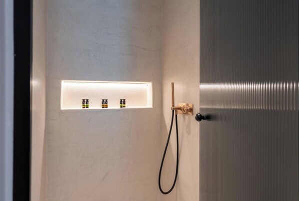 A bathroom with a white wall, a towel rack, and a showerhead. - Muse of Mykonos (Mykonos)