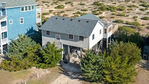 A coastal house with a balcony, surrounded by trees and a view of the ocean.