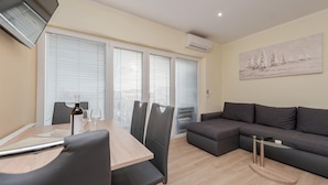 A modern living room with a dining area, featuring a sofa, a dining table with chairs, and a painting on the wall.