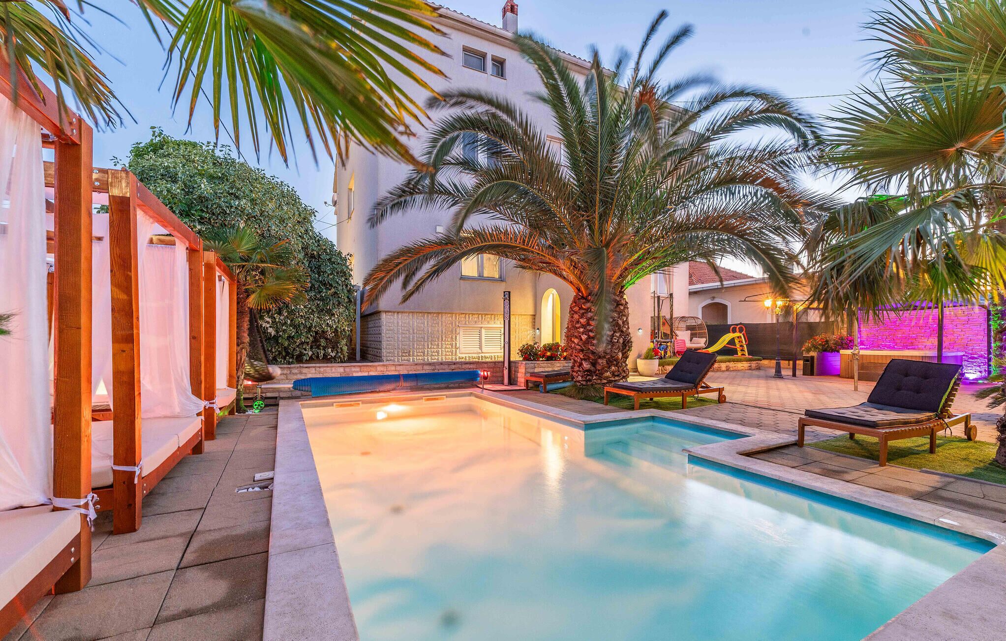 A swimming pool with lounge chairs, a wooden pergola, and a palm tree.