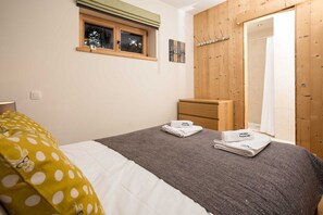 A bedroom with a bed, a dresser, a window, and a wooden wardrobe.