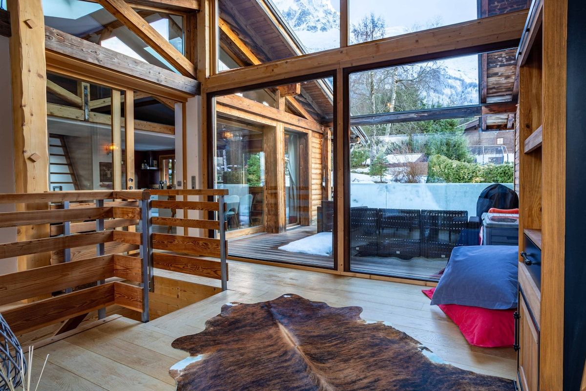 Un interior de madera con un amplio ventanal que da al exterior, un banco de madera y una alfombra de cuero.