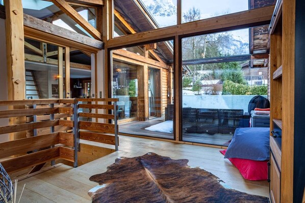 A wooden interior with a large glass door leading outside, a wooden bench, and a leather rug.