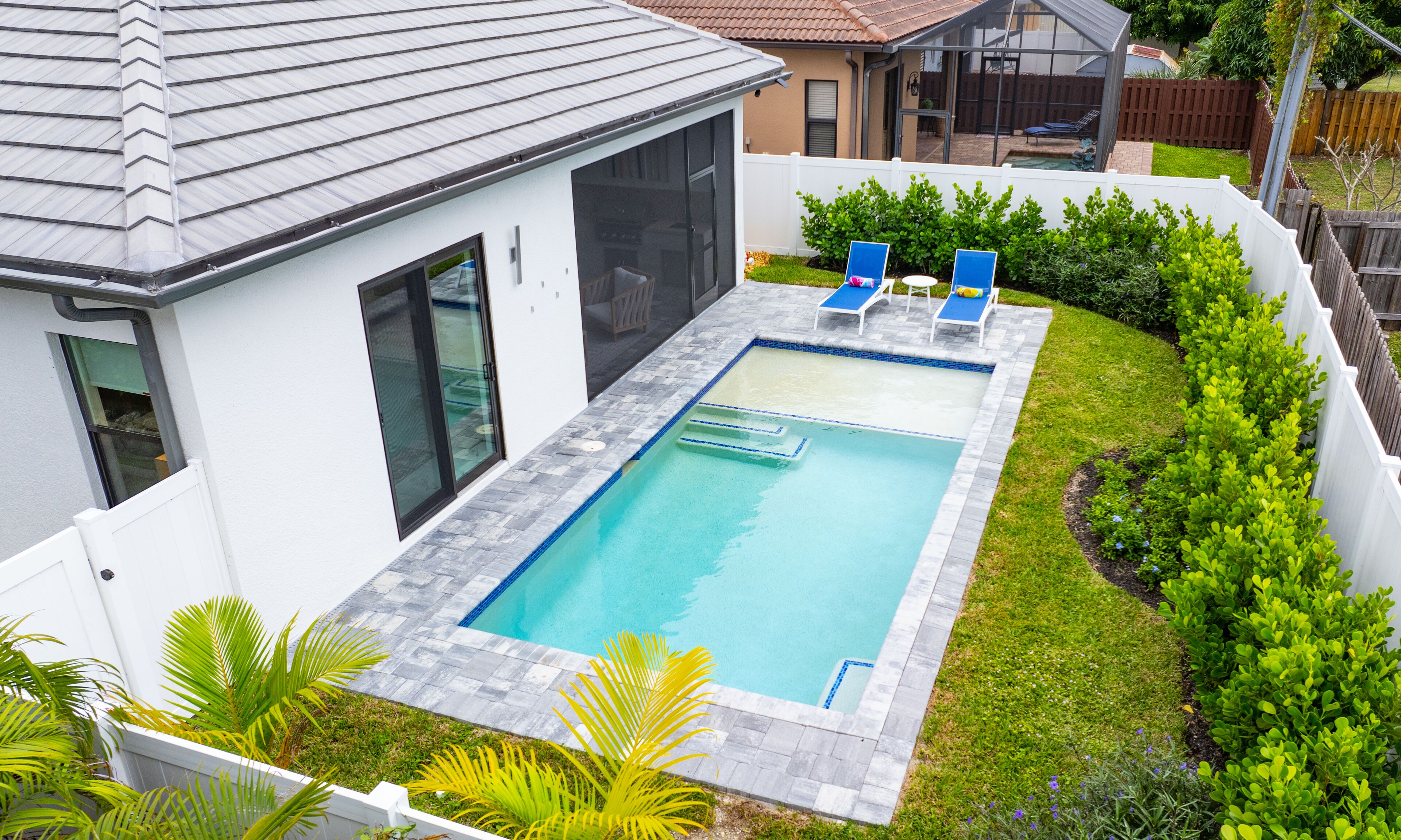 A rectangular swimming pool with a tiled deck, two lounge chairs, and a small garden area with plants.