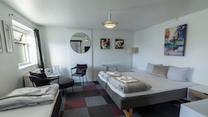 A modern hotel room with a bed, a desk, a chair, a small table, and a large mirror. - Hotel Rønne H (Ronne)