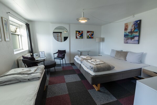 A modern hotel room with a bed, a desk, a chair, a small table, and a large mirror.