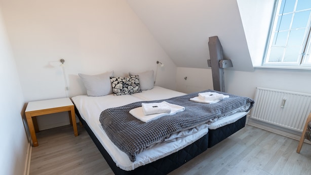 A bedroom with a bed, bedside tables, a window, and a radiator. - Hotel Rønne H (Ronne)