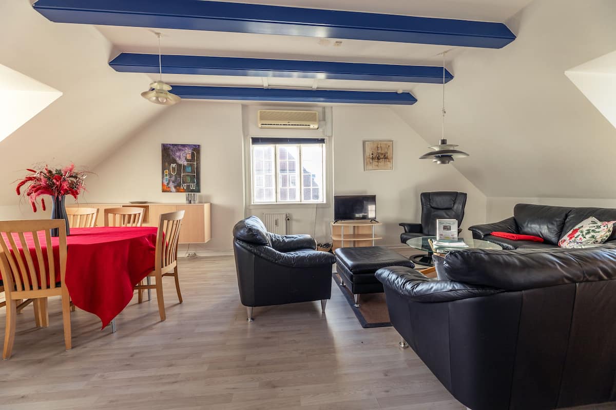 Ein modernes Wohnzimmer mit Essbereich, ausgestattet mit einer roten Tischdecke, schwarzen Ledersofas und einem Holzessttisch.