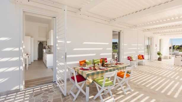 An outdoor dining area with a table set for four, surrounded by white chairs with colorful cushions. - 3675 Dimora Seculari by Perle di Puglia (Mesagne)
