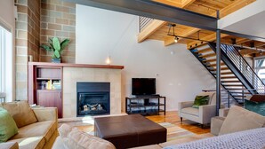 A spacious living room with a fireplace, comfortable seating, a television, and a staircase leading to an upper level.