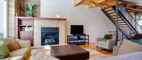 A spacious living room with a fireplace, comfortable seating, a television, and a staircase leading to an upper level.
