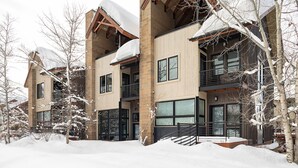 A modern multi-story building with large windows and balconies, surrounded by snow-covered trees.