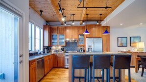 A modern kitchen with wooden cabinets, a stainless steel refrigerator, and a bar area with stools.