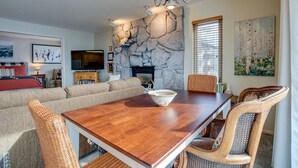 Uma sala de jantar com lareira de pedra, mesa de madeira e cadeiras de vime.